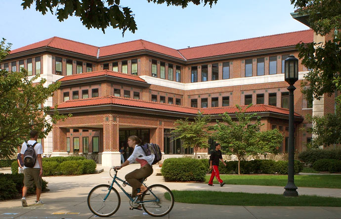 a student rides a bike in front of Schleman Hall